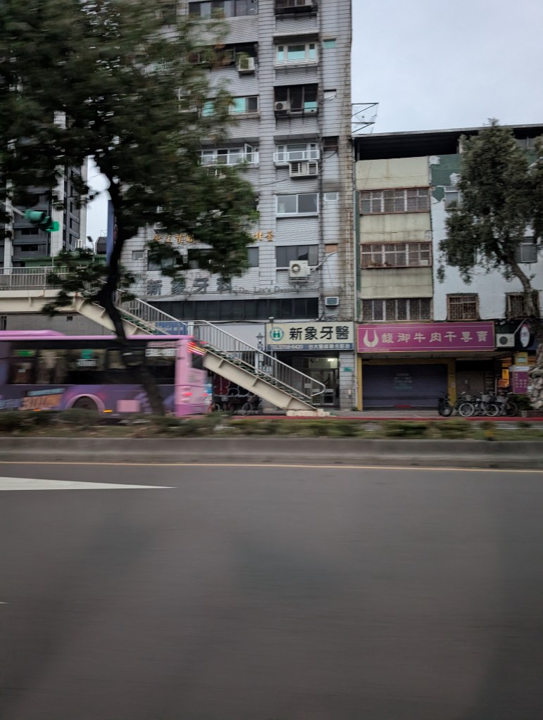 the street view of Taipei, includes a couple of buildings and a blurry bus as it goes by